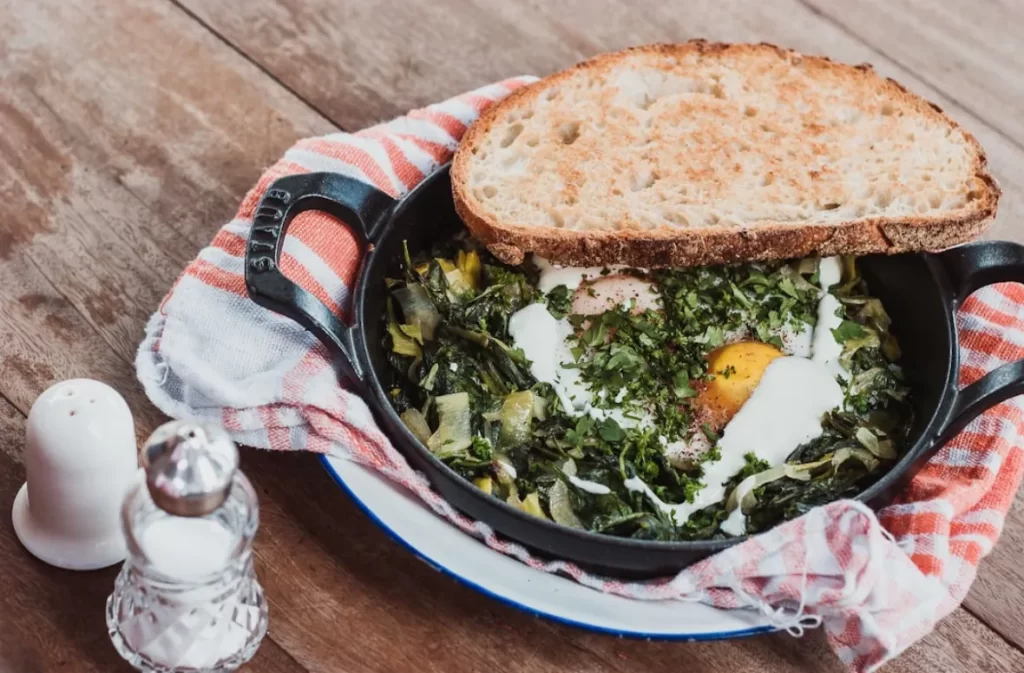 Skillet with greens, eggs, and toasted bread.
