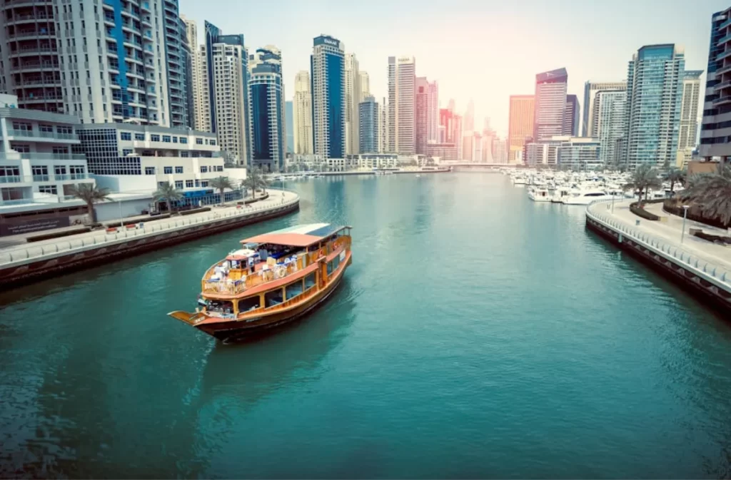 A wooden boat cruising in a modern city marina.