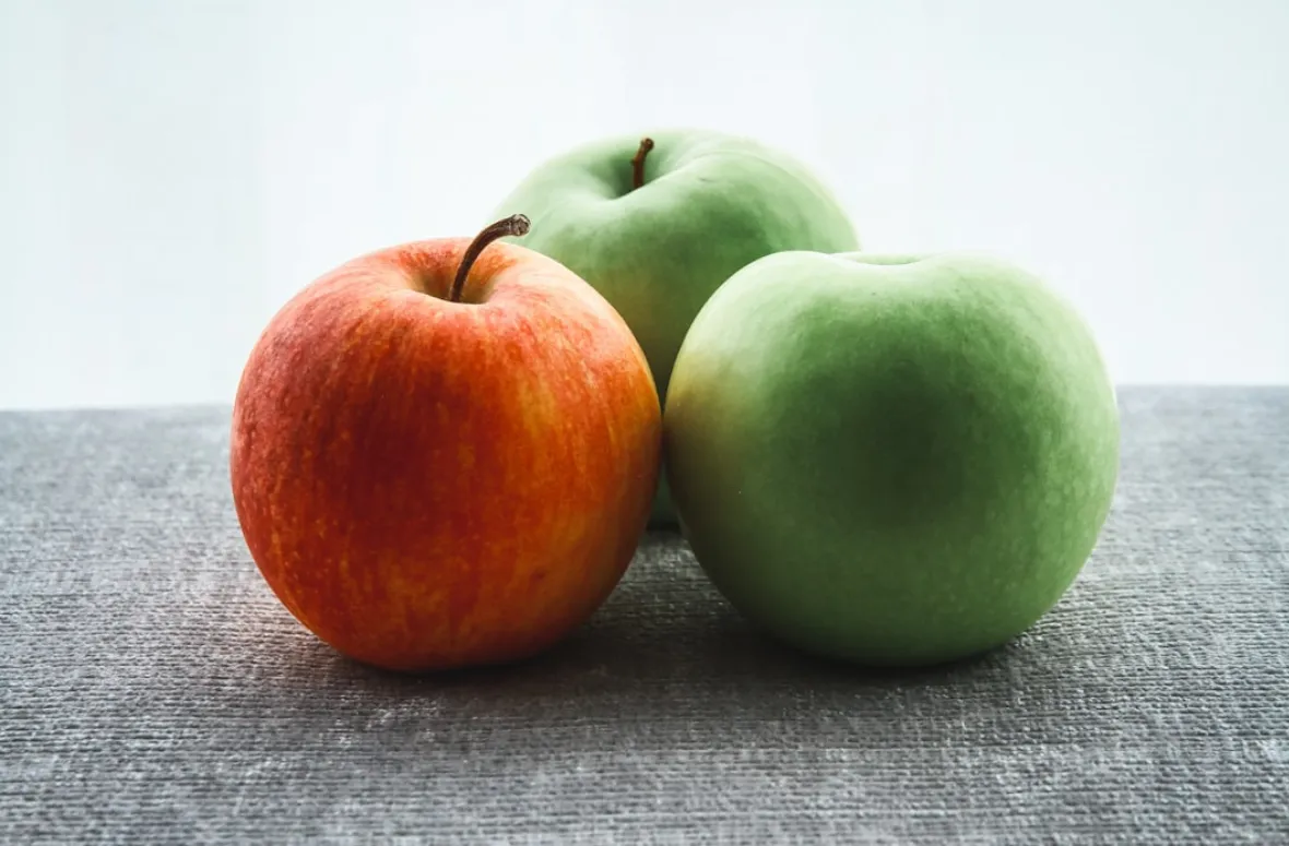 Red apple with two green apples on a tablecloth.