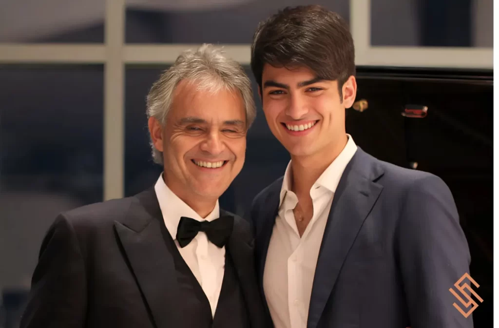 Andrea Bocelli and a young man smiling in formal suits.