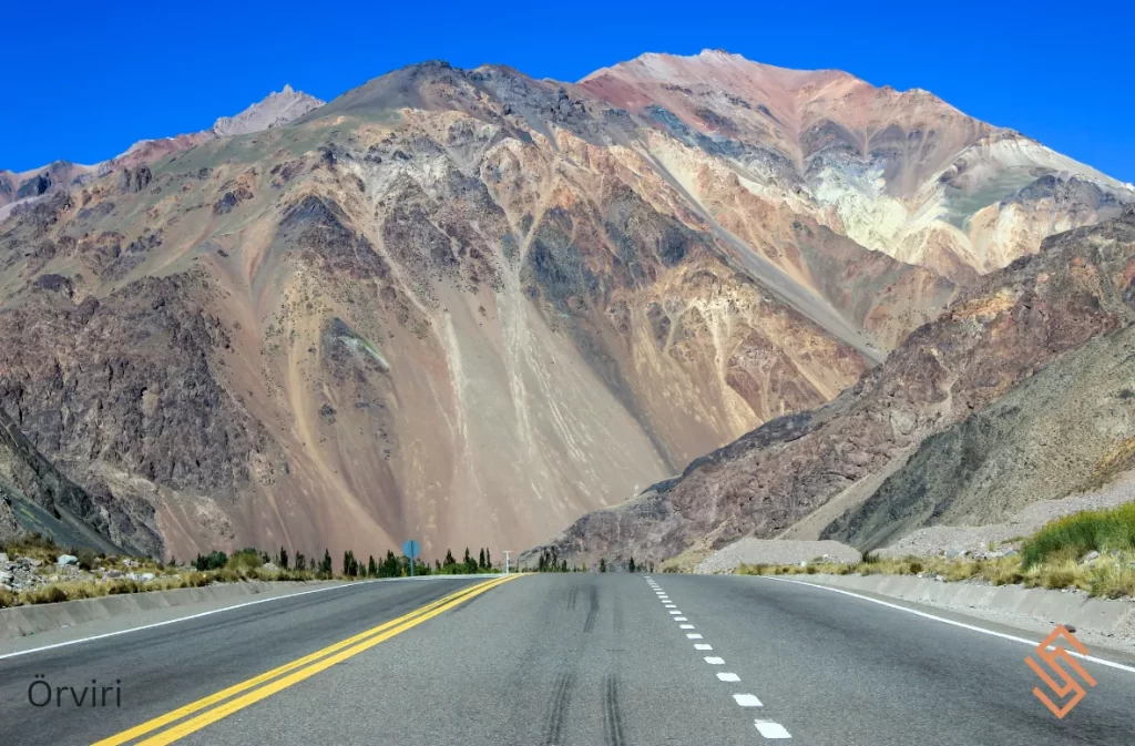 A highway stretching towards rugged mountains under a clear blue sky.