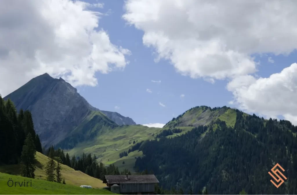 A mountain cabin nestled in a green valley under a bright sky.