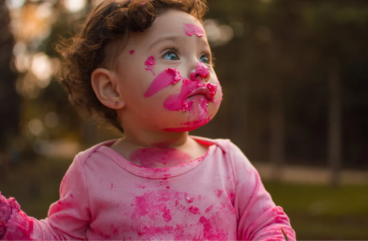 Toddler with pink paint on face learning humor through creativity.