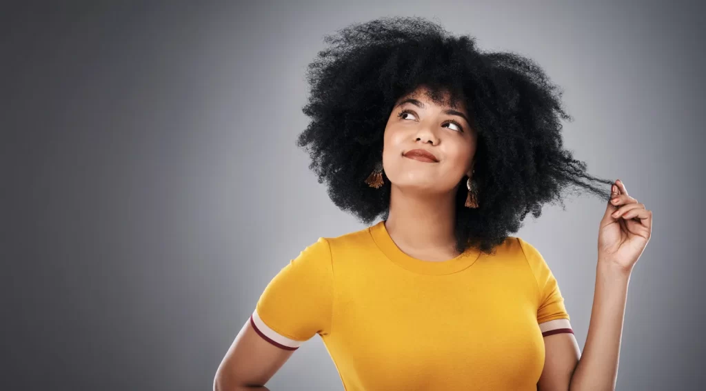 Woman with afro-textured hair looking thoughtful, holding a strand.