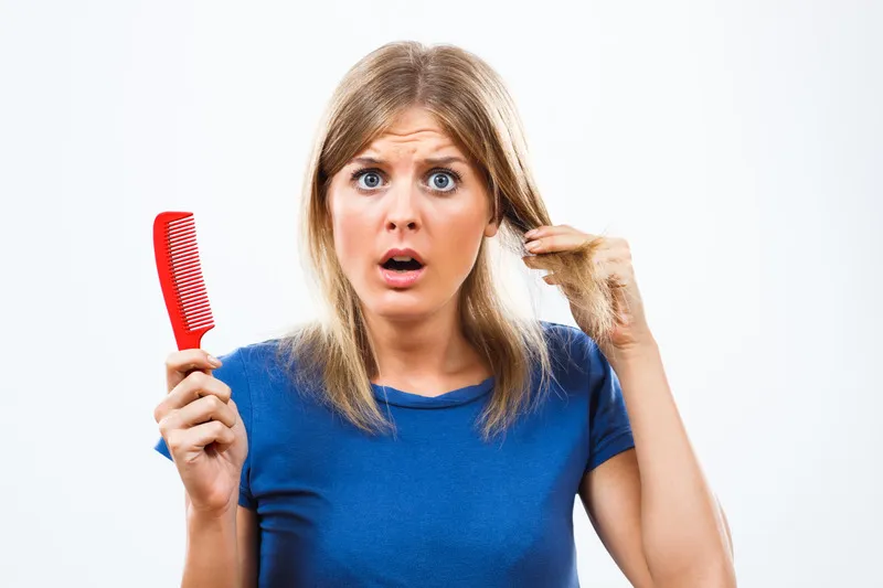 Shocked woman with blonde hair, struggling to comb tangles.