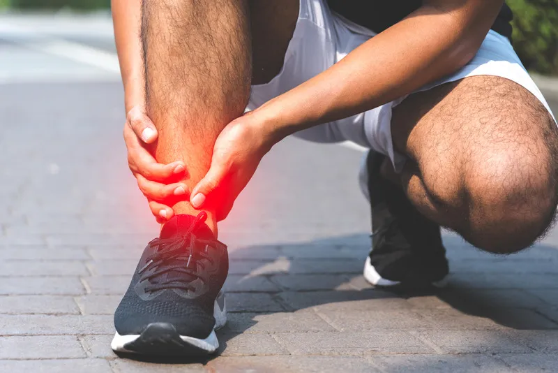 Individual kneeling with hands on an injured foot, indicating a possible break.