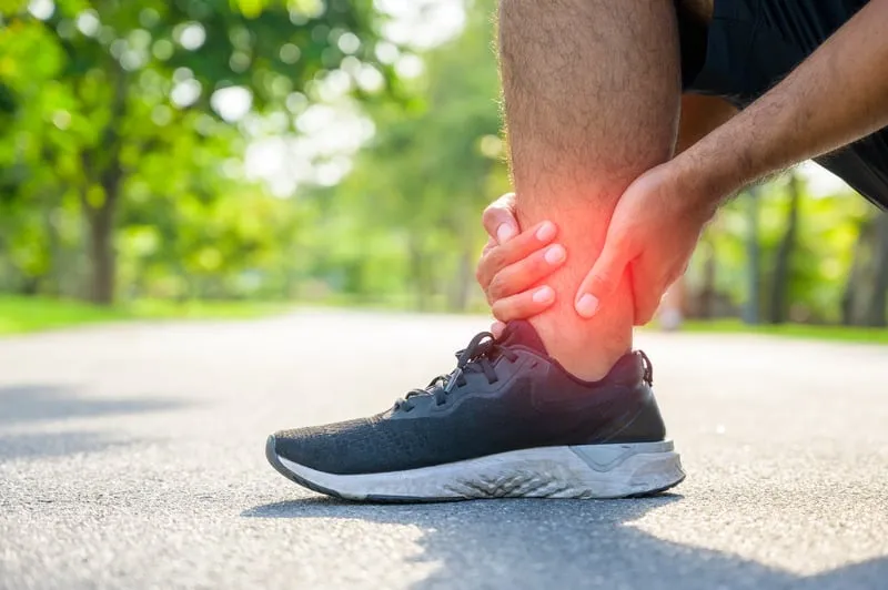 Person clutching their ankle with visible pain on a running track.