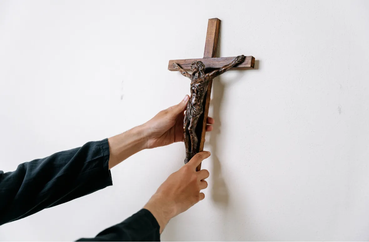 A wooden crucifix being hung on a white wall.