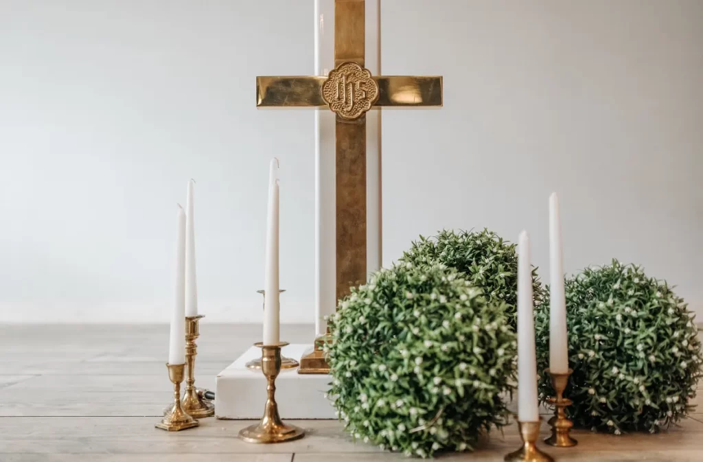 A golden altar cross with candles and greenery.